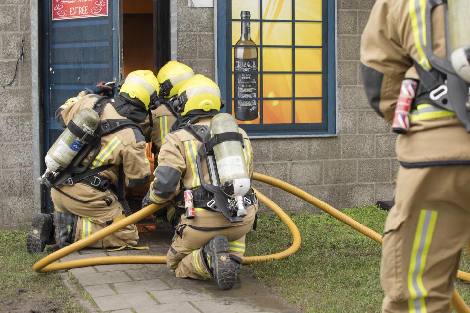 Brandweermannen blussen een brand vanuit de deuropening
