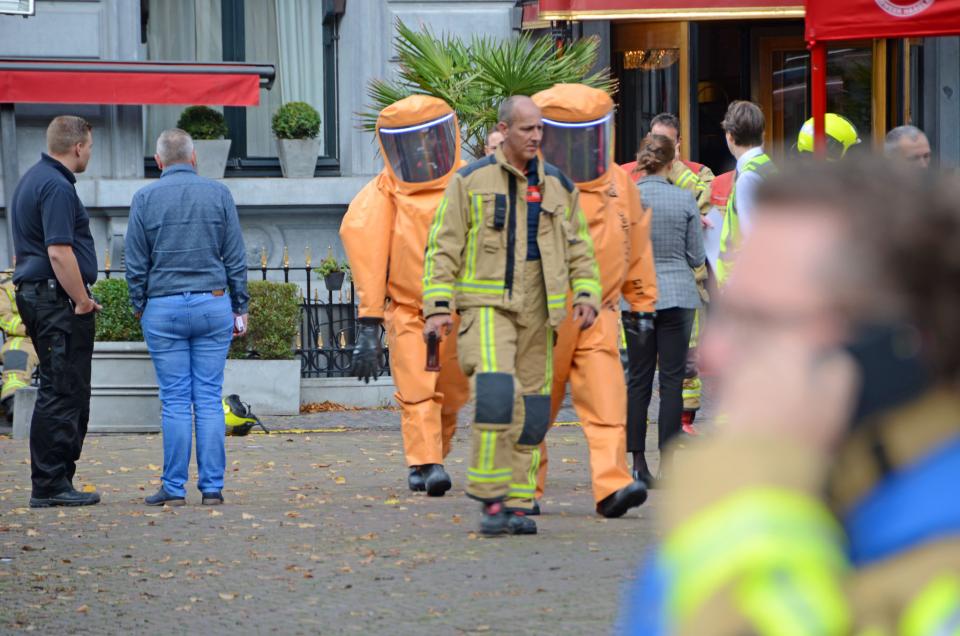 Brandweerman en twee personen in beschermende pakken lopen op straat tussen een groep mensen.